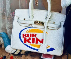 Eine Handtasche in der Form einer Birkin-Bag ist im Stil des Burger-King-Logos mit Bur Kin beschriftet.